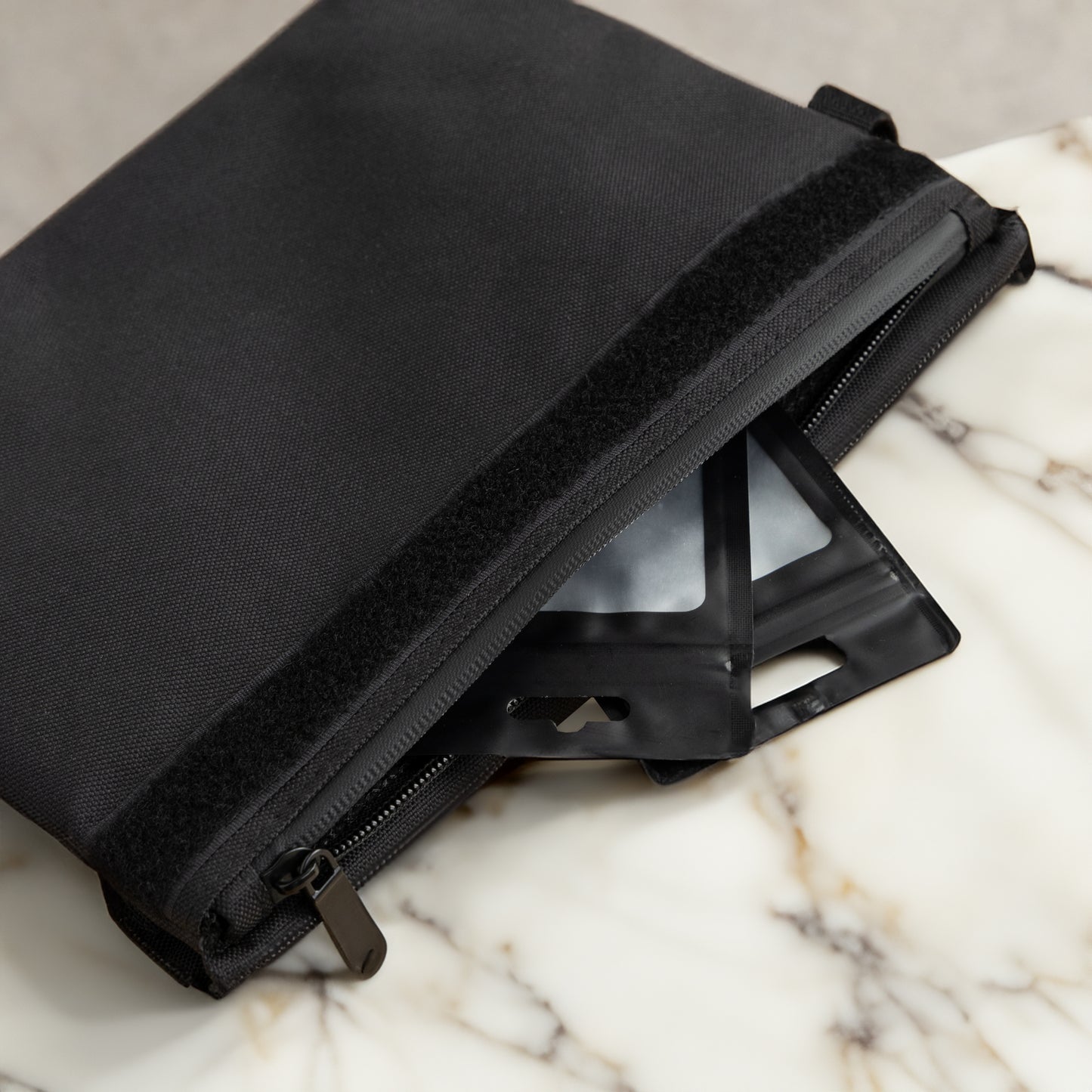 Close-up of a black Coast Angels Soho smell-proof pouch unzipped on a marble surface, revealing two sleek black resealable bags inside, highlighting discreet, functional storage.