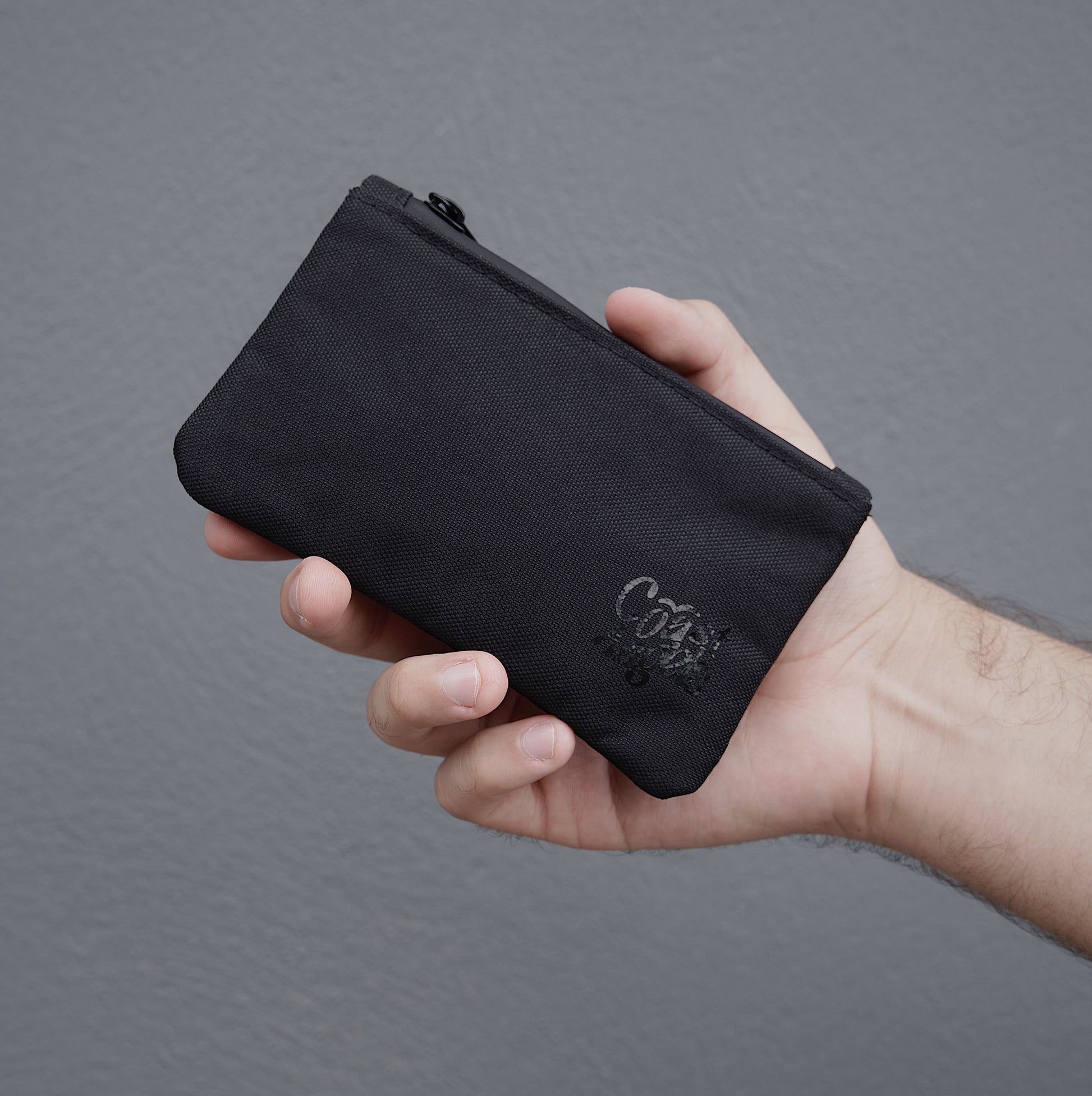 Hand holding the Coast Angels Camden Smell Proof Pouch, providing size reference and showcasing its compact, portable design.