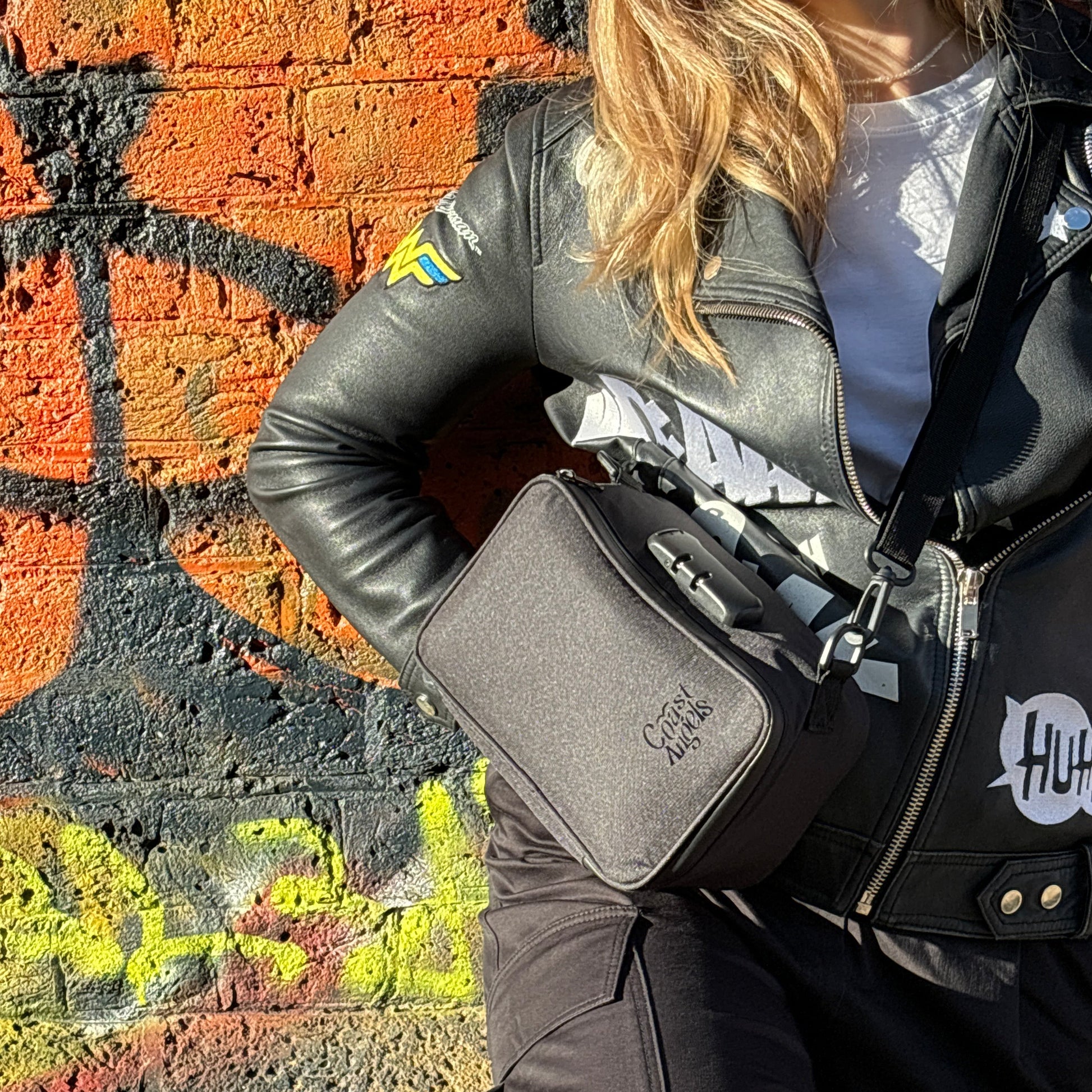 Woman wearing the Coast Angels Dalston Bag, standing against a colorful wall, showcasing the bag's stylish and discreet design.