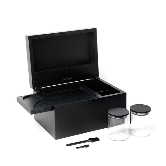 A black wooden Coast Angels storage box with its lid open, shown on a white background with two clear glass jars and two small black accessories.