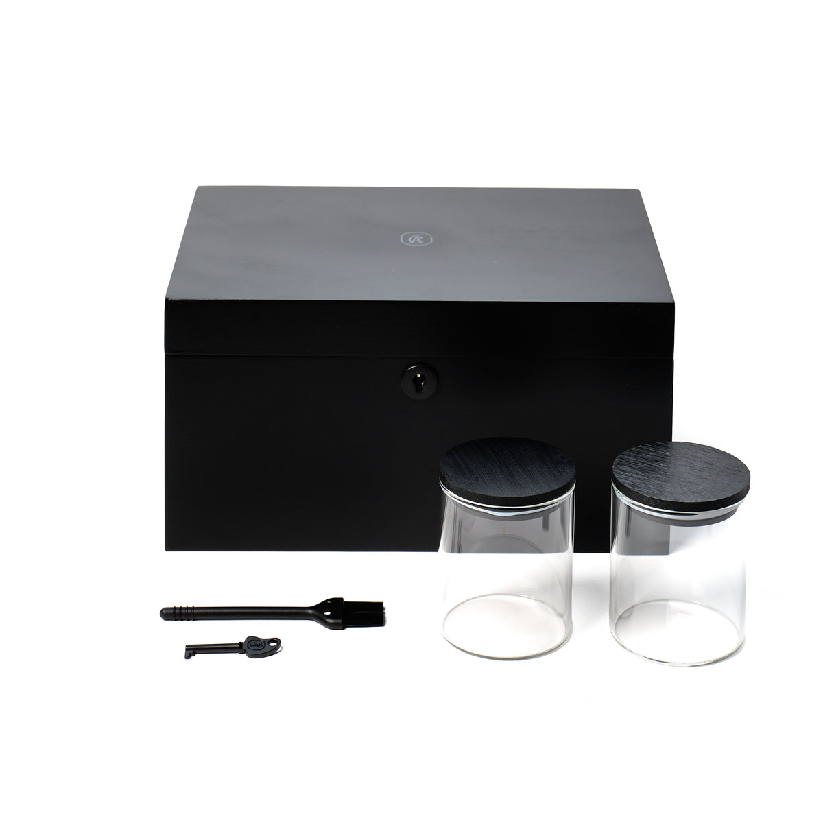 A black bamboo storage box with a small key and a black brush, shown with two clear glass jars with dark lids in front, on a white background.