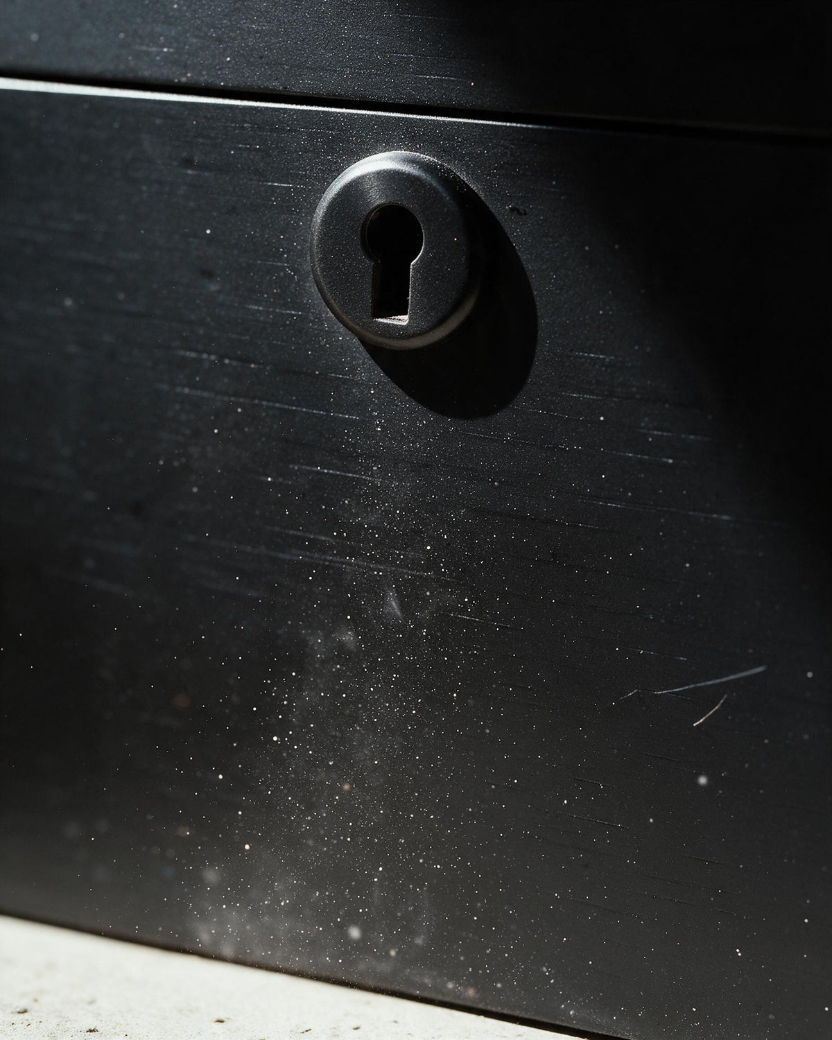 Close-up of a black metal safe or box with a round keyhole and a small key inserted, set against a dark background with bright sunlight and shadows.