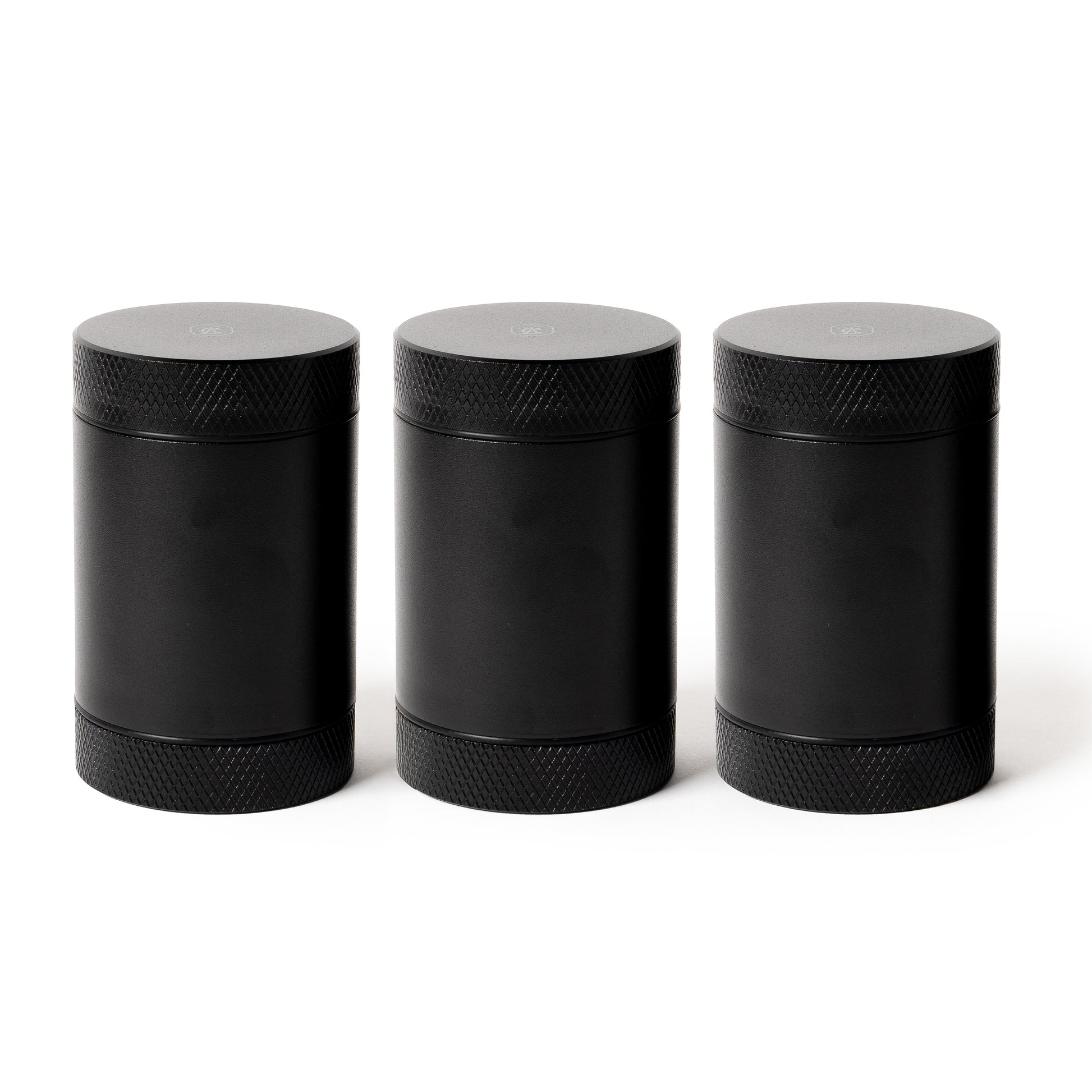 Three black Coast Angels cylindrical containers with textured lids on a white background